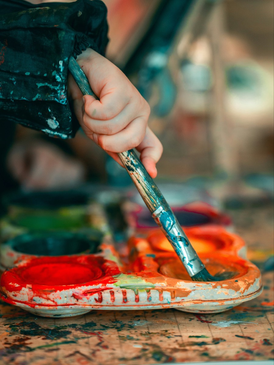 Une main d’enfant trempe un pinceau dans une palette de peinture