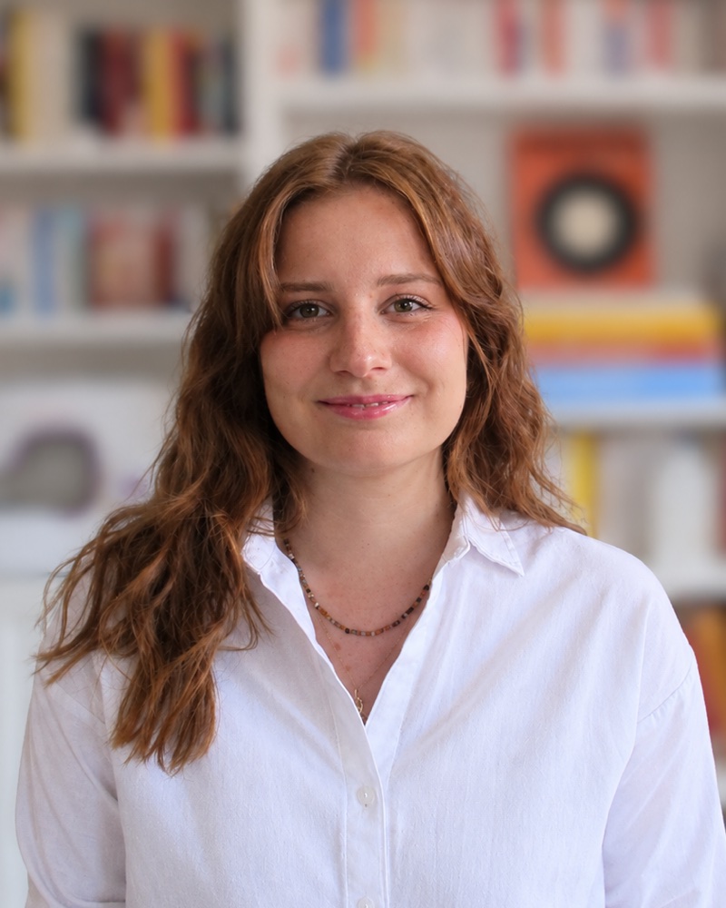 Clara Esaltato, souriante, devant une bibliothèque